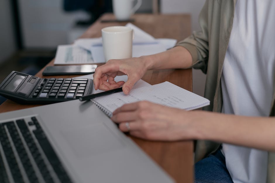 Person writing on a notepad next to a laptop and a cup of coffee, symbolising questions.